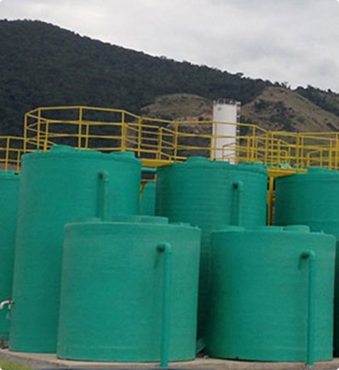 ETE pré-fabricada com tanques verdes e passarela amarela, ao pé de um morro